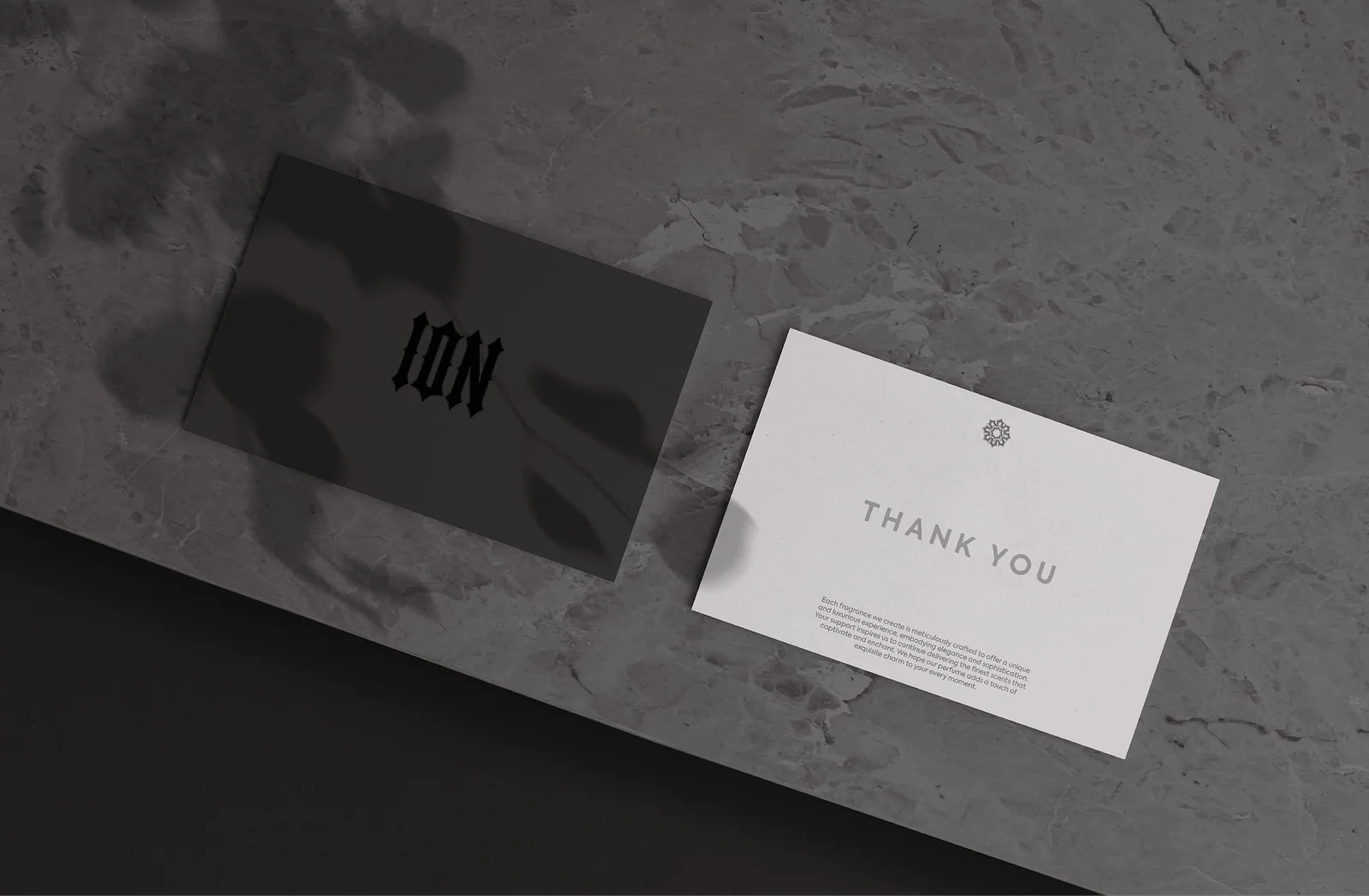 Grey business card and white thank-you card on a stone surface