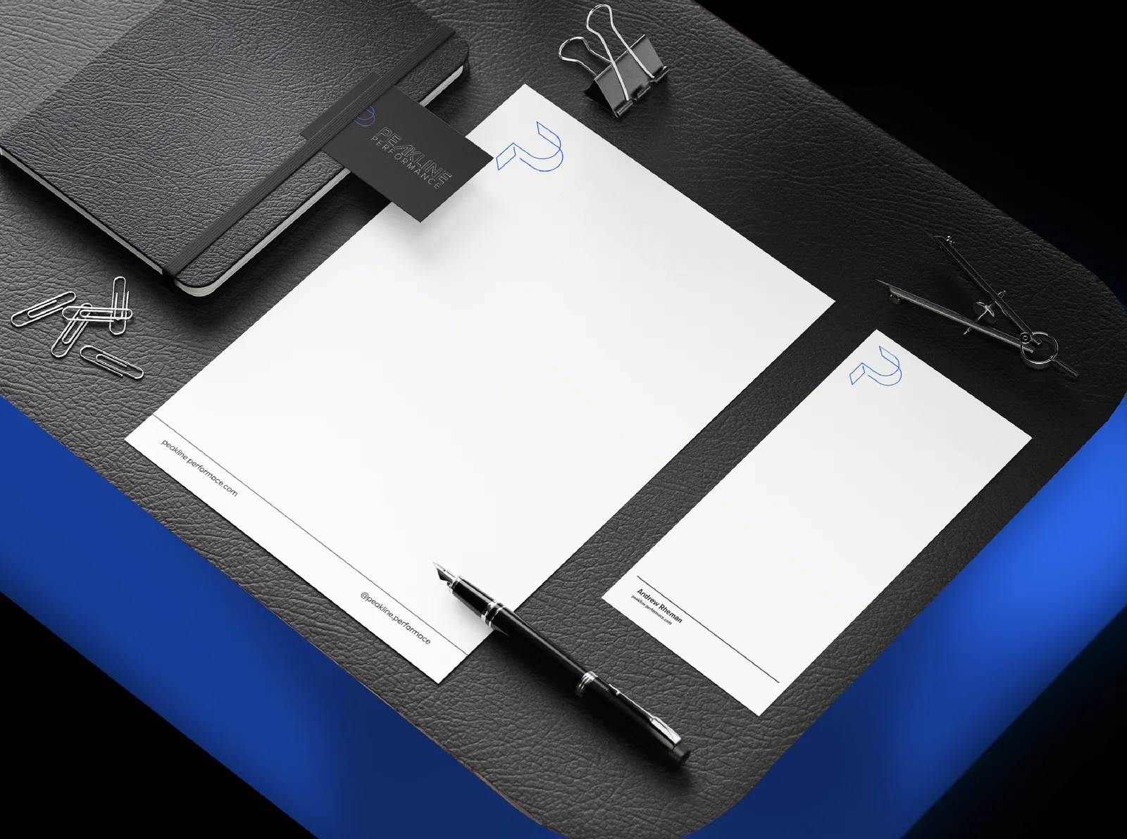 Dark stationery flat lay with letterheads, a pen and a blue desk mat