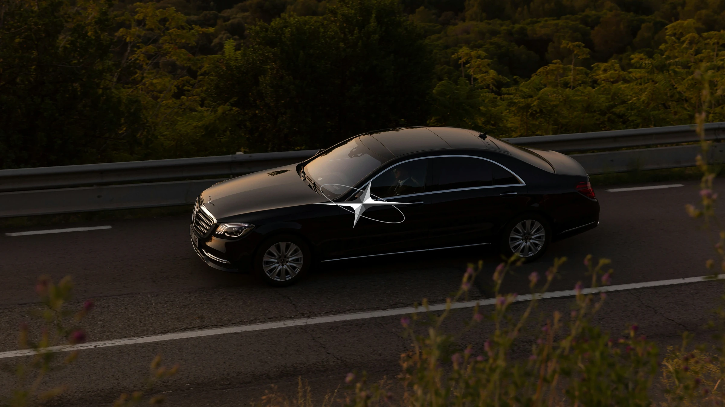 Black luxury saloon car on a tree-lined highway at dusk
