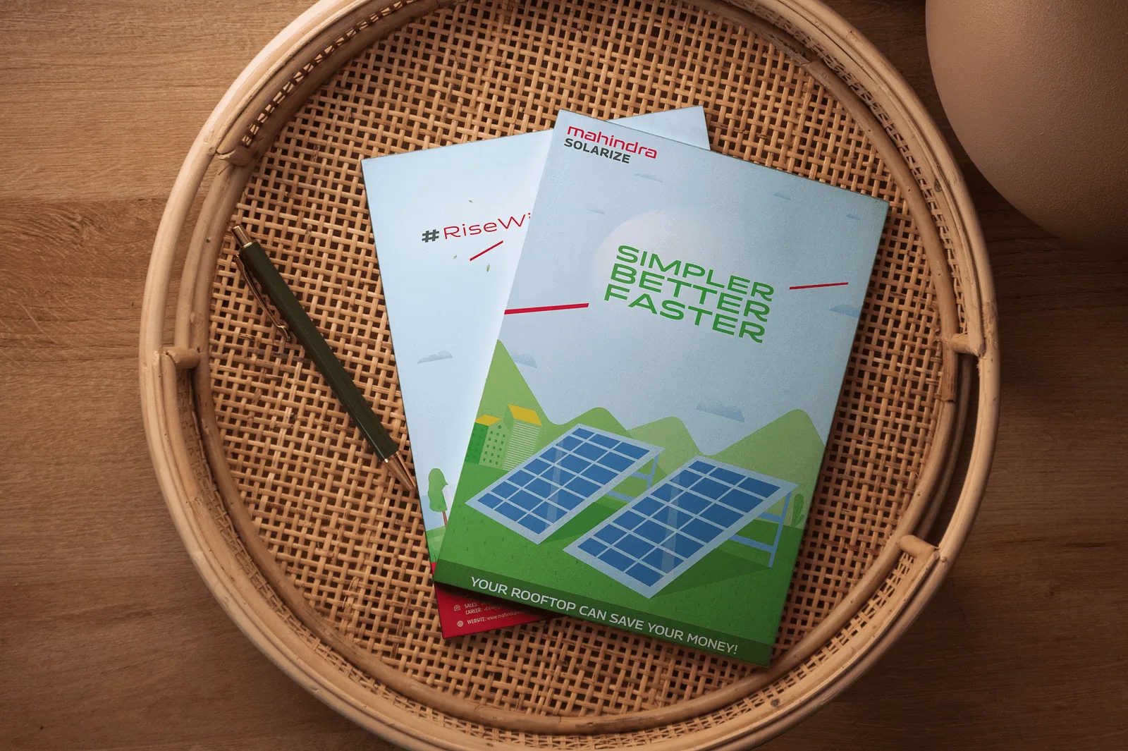 Two Mahindra Solarize brochures in a woven tray on a wooden table