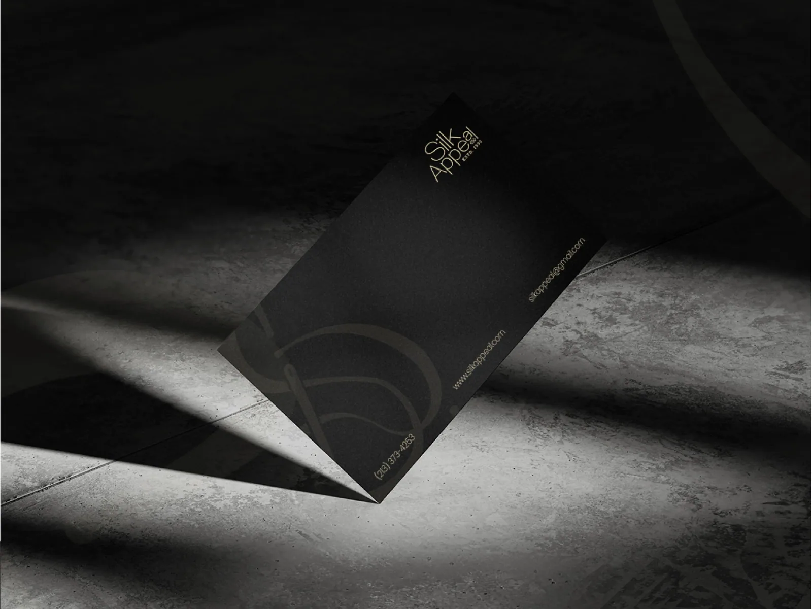 Dark business card in raking light showing the embossed monogram